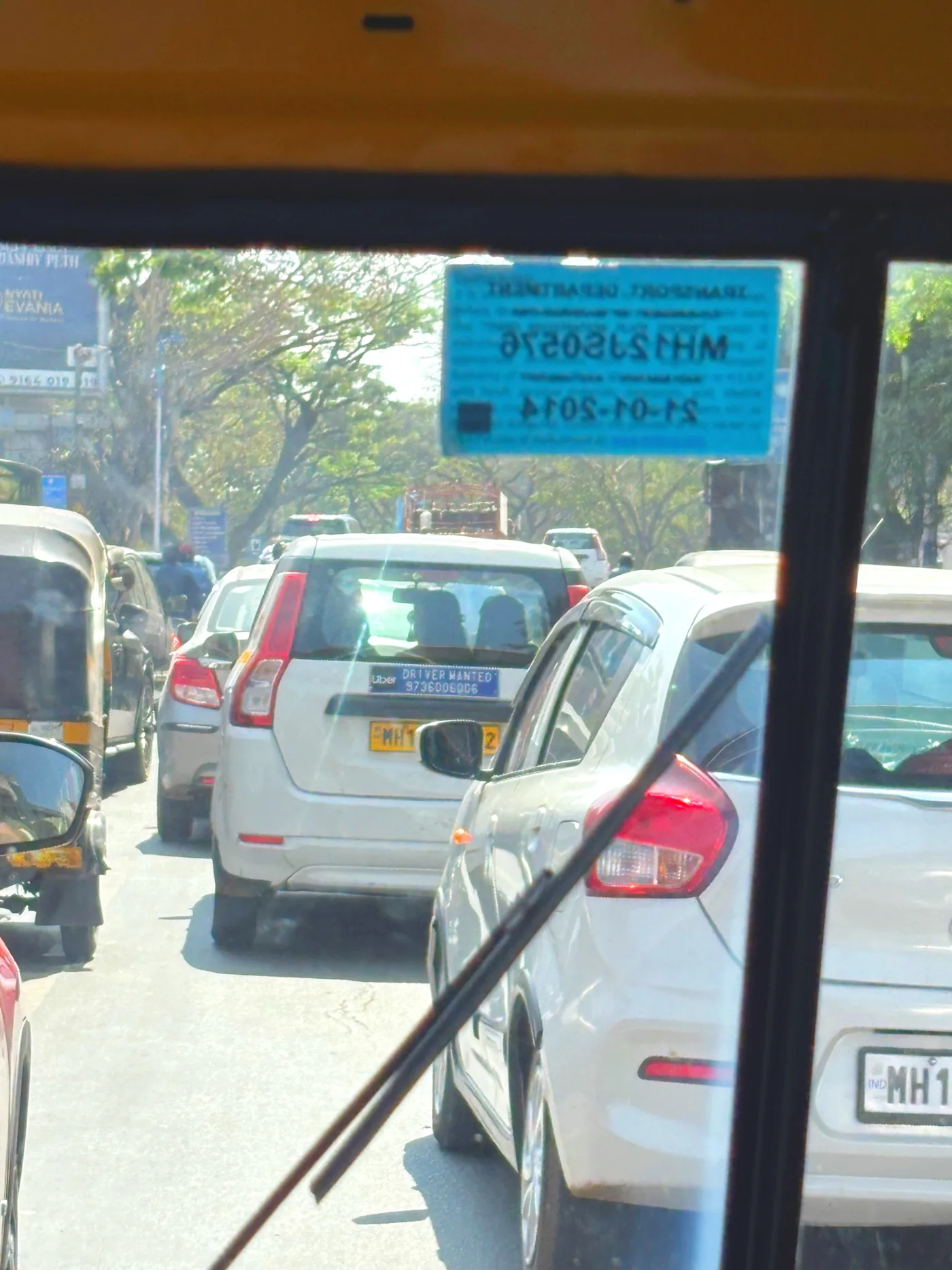 Traffic seen through the front of the auto rickshaw, a transport permit stuck to the windscreen