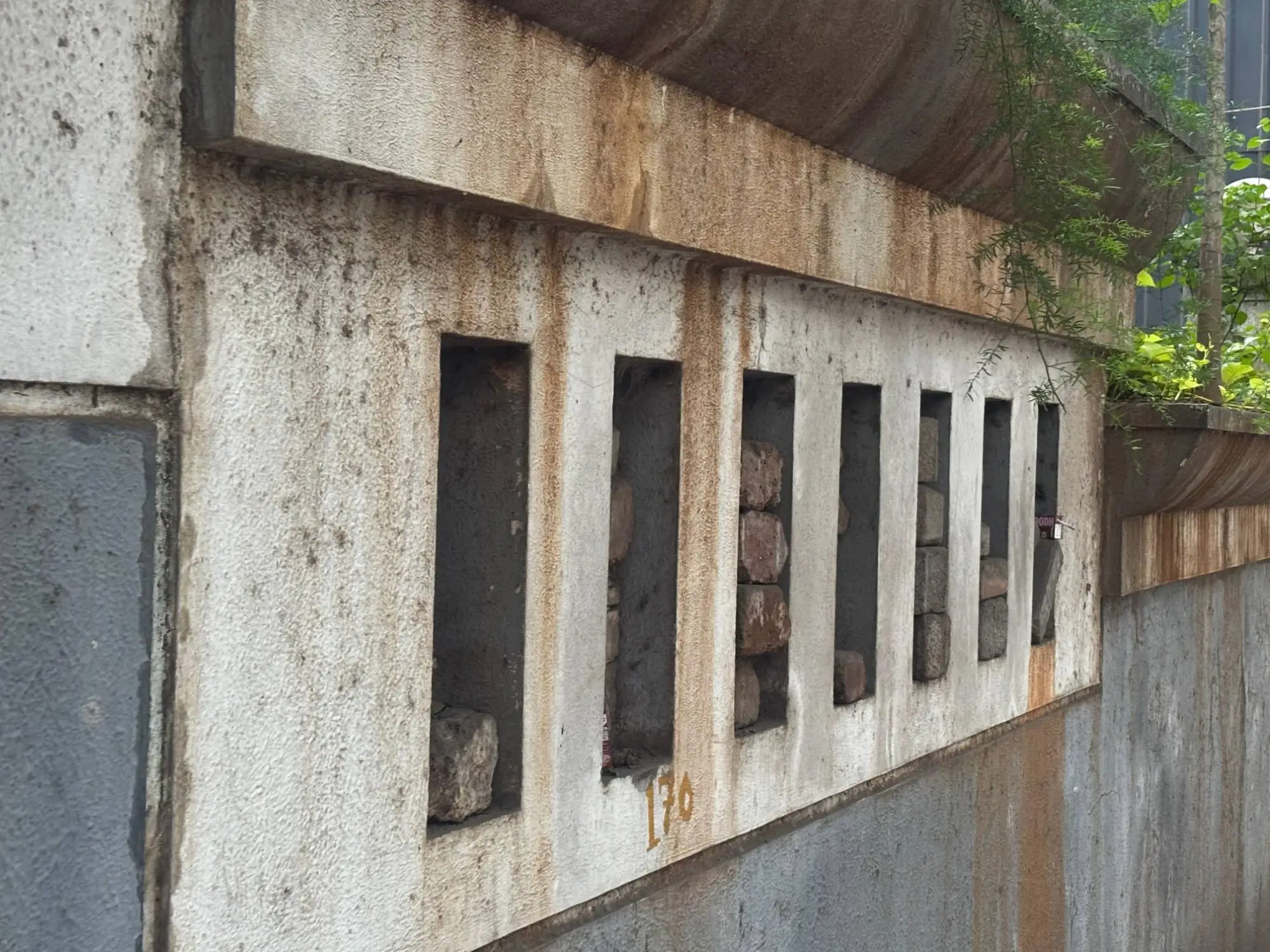 A weathered concrete wall streaked with rust, its row of openings stacked with bricks, numbered 170