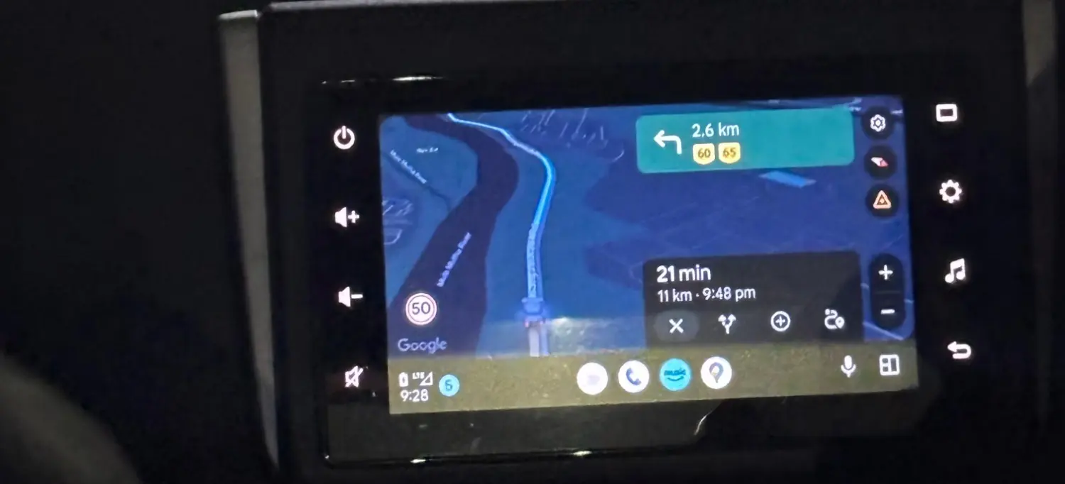 The car’s dashboard screen showing the route: a left turn in 2.6 km, 21 minutes and 11 km to go