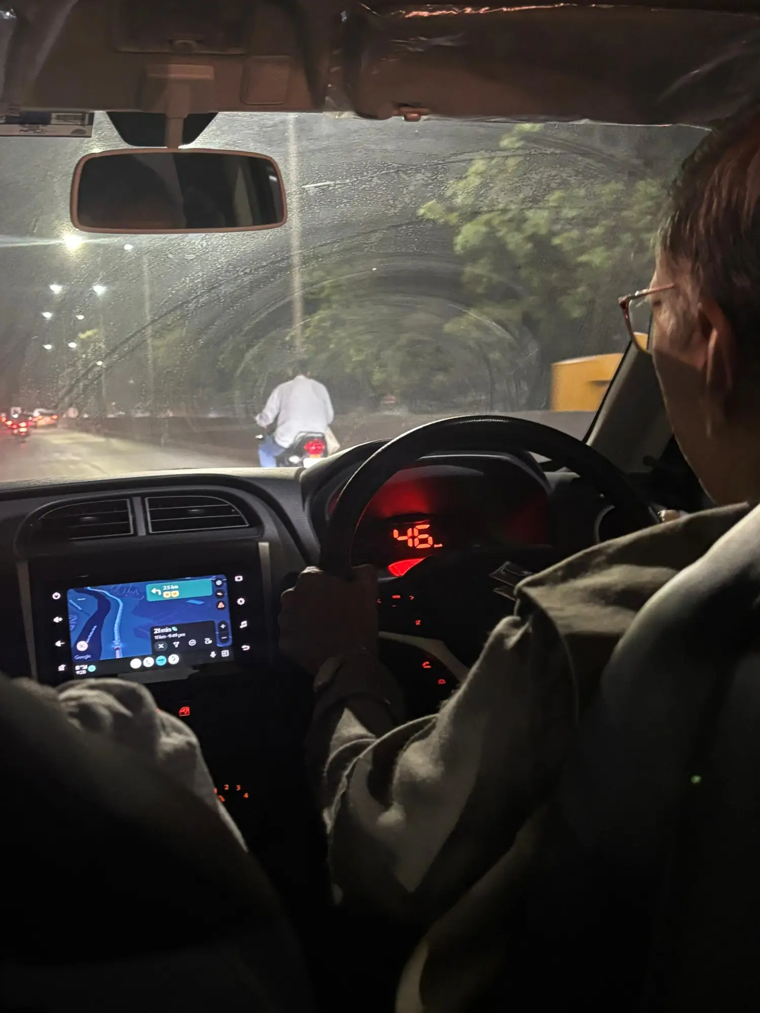 Inside the car at night: rain on the windscreen, the driver at the wheel, the route glowing on the dashboard screen